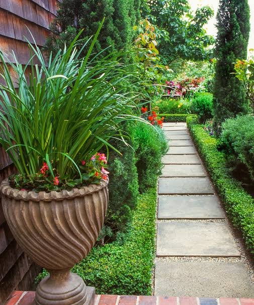 Stone path through a narrow side yard garden with potted plants and trimmed hedges, a space suited to artificial turf in the San Fernando Valley